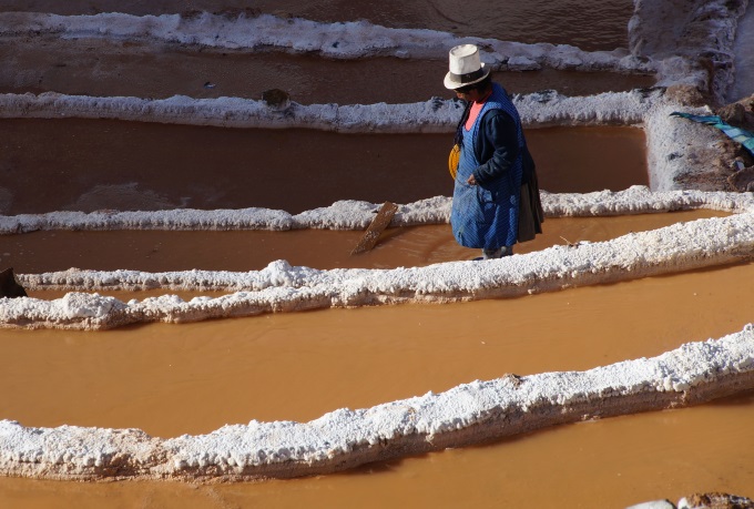 A traditional worker harvesting pink salt in the evaporation ponds in Maras with a sief