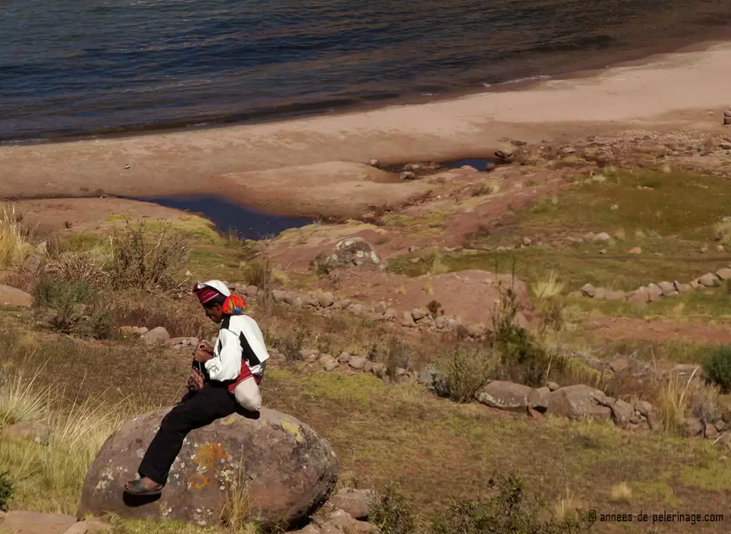 A man knitting a hat sitting on a big stone on Taquile island lake titicaca peru