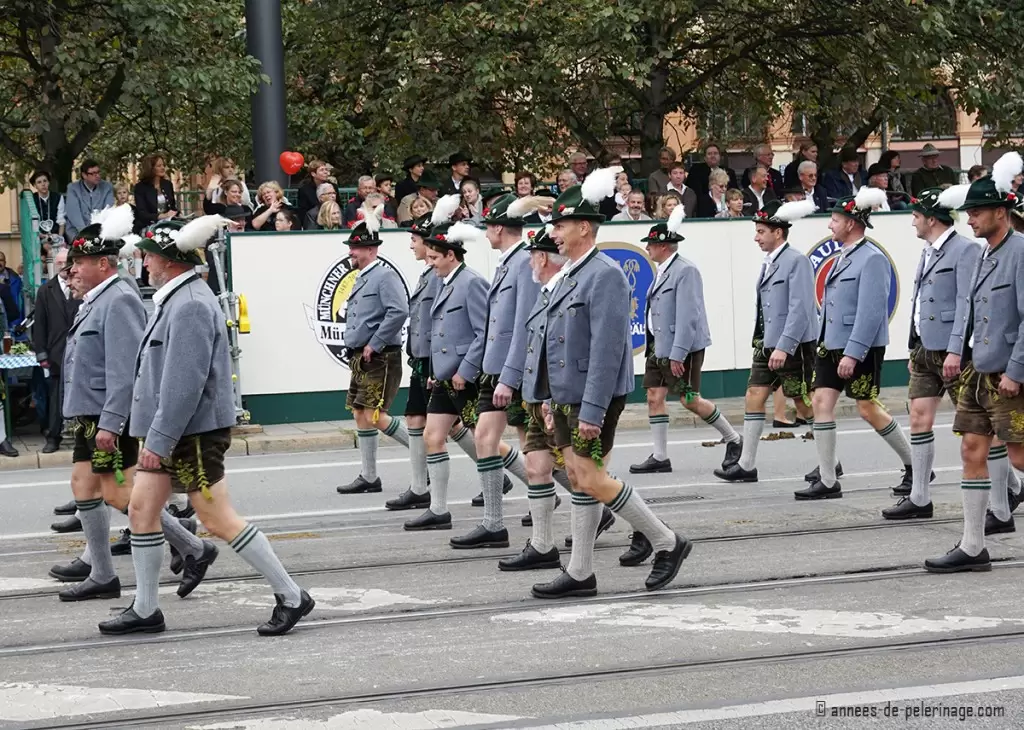 A group of men wearing traditional bavarian lederhosen and hats with white feathers for the costume parade in munich