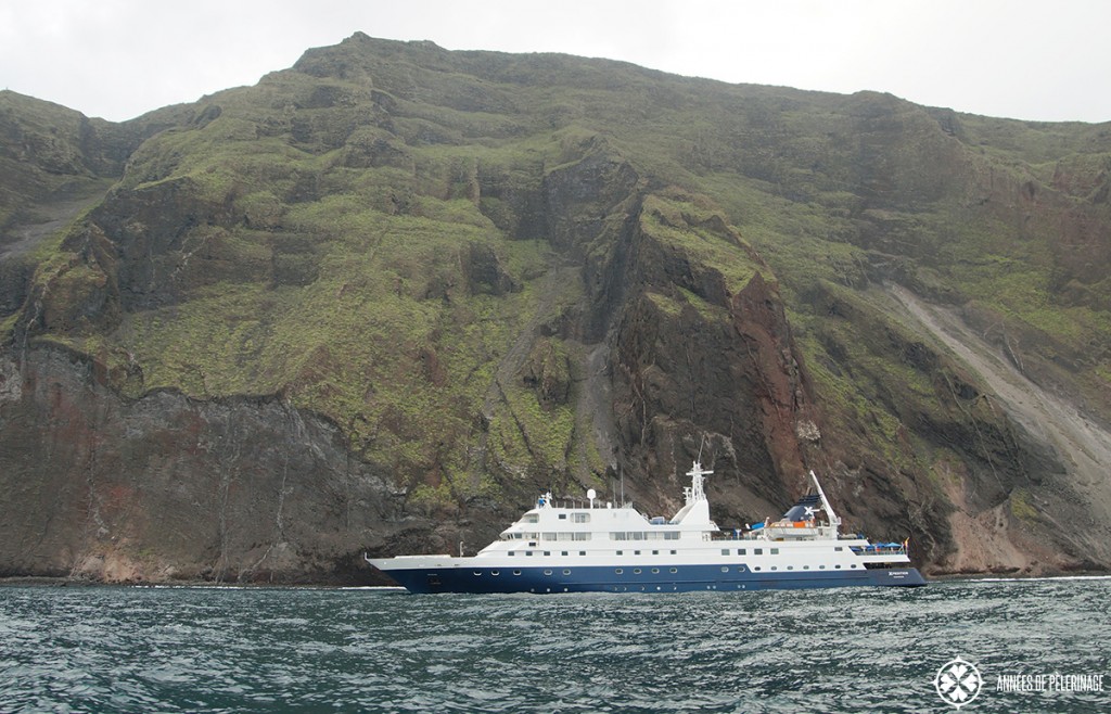 The Celebrity Xpedition Galapagos luxury cruise ship in front massive volanic rock formations