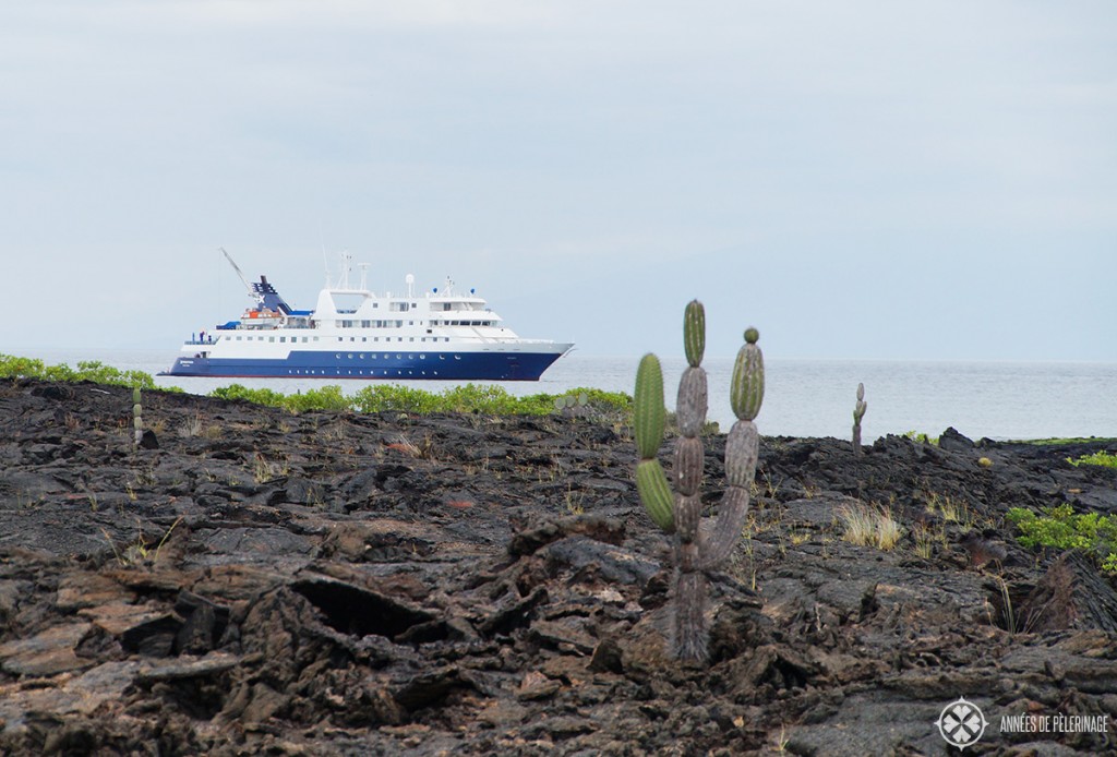 The Celebrity Xpedition Galapagos luxury cruise ship in the background - some lava formations in the foreground