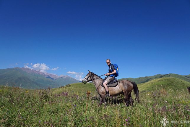 Horse riding in Kyrgyzstan over a high mountain pass among a beautiful blooming meadow.