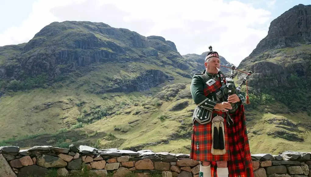 Glen Coe in Scotland and man playing bag pipes