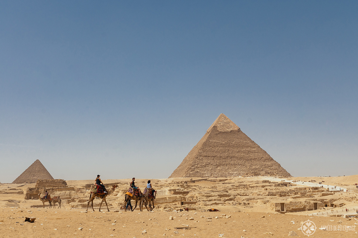 The pyramid of Khafre with the pyramid of Menkaure in the background and a couple of camels and the Giza necropolis in the foreground.