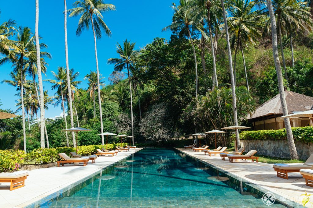 The big pool at the beach club of the Amankila luxury hotel with big palm trees offering shade