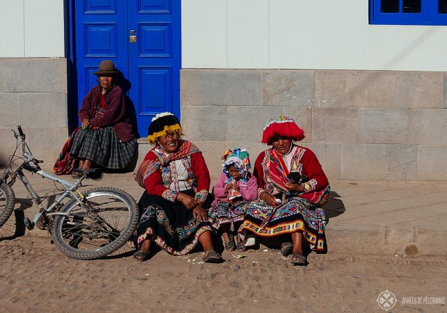 Locals in traditional andean clothing sitting on the sidewalk in Pisac's old town