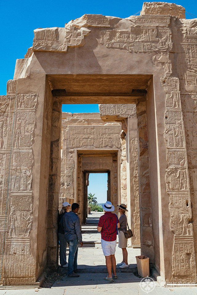 Tourist listening to a tourist guide in the shade of an ancient arch - summer is not the best time to visit Egypt, as it can get incredibly hot around the many ancient temples