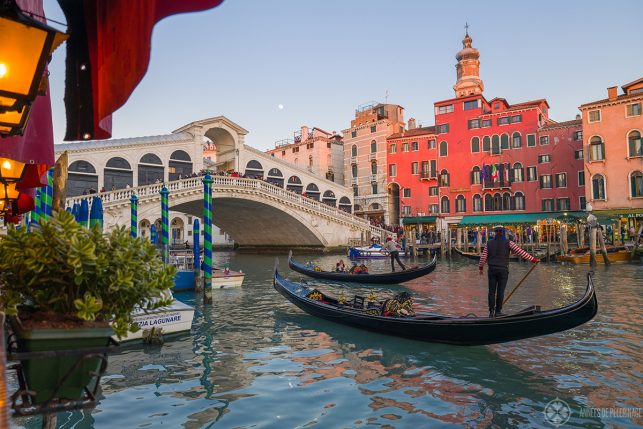 A gondola with a gondolier in a red-white striped shirt in front of the rialto bridge