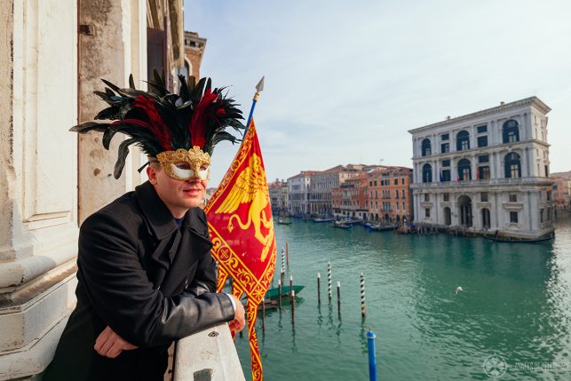 Me wearing a carnival mask with black and red feathers on the balcony of the Aman venice hotel at the Canal Grande