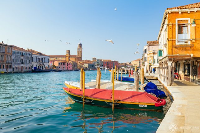 View along the main water channel through the Island of Murano near Venice with three storied colorful houses on each side an a couple of boats in the foreground