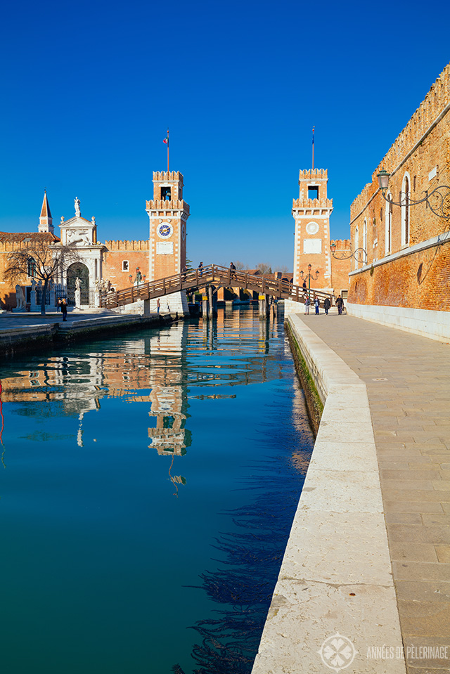 The entrance of the Venetian arsenal with two red brick towers to each side of the water channel and a bridge across it