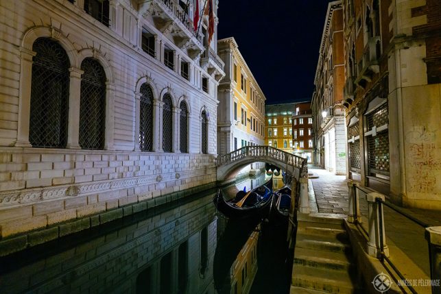 a beautiful little canal with a marble bridge and a palace in Venice at night