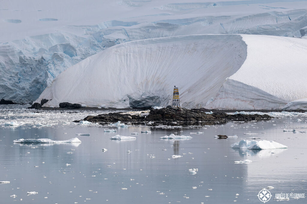 a small lighthouse on an isolated rock with a glacier in the backgruond