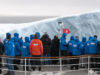 What to pack for Antarctica passengers standing on the bow of a cruise ship to touch an ice berg