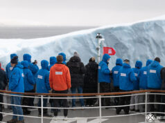 What to pack for Antarctica passengers standing on the bow of a cruise ship to touch an ice berg